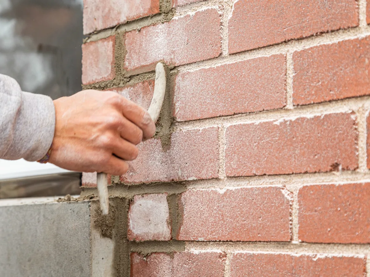 Tooling fresh mortar into a raked-out joint on a red brick wall