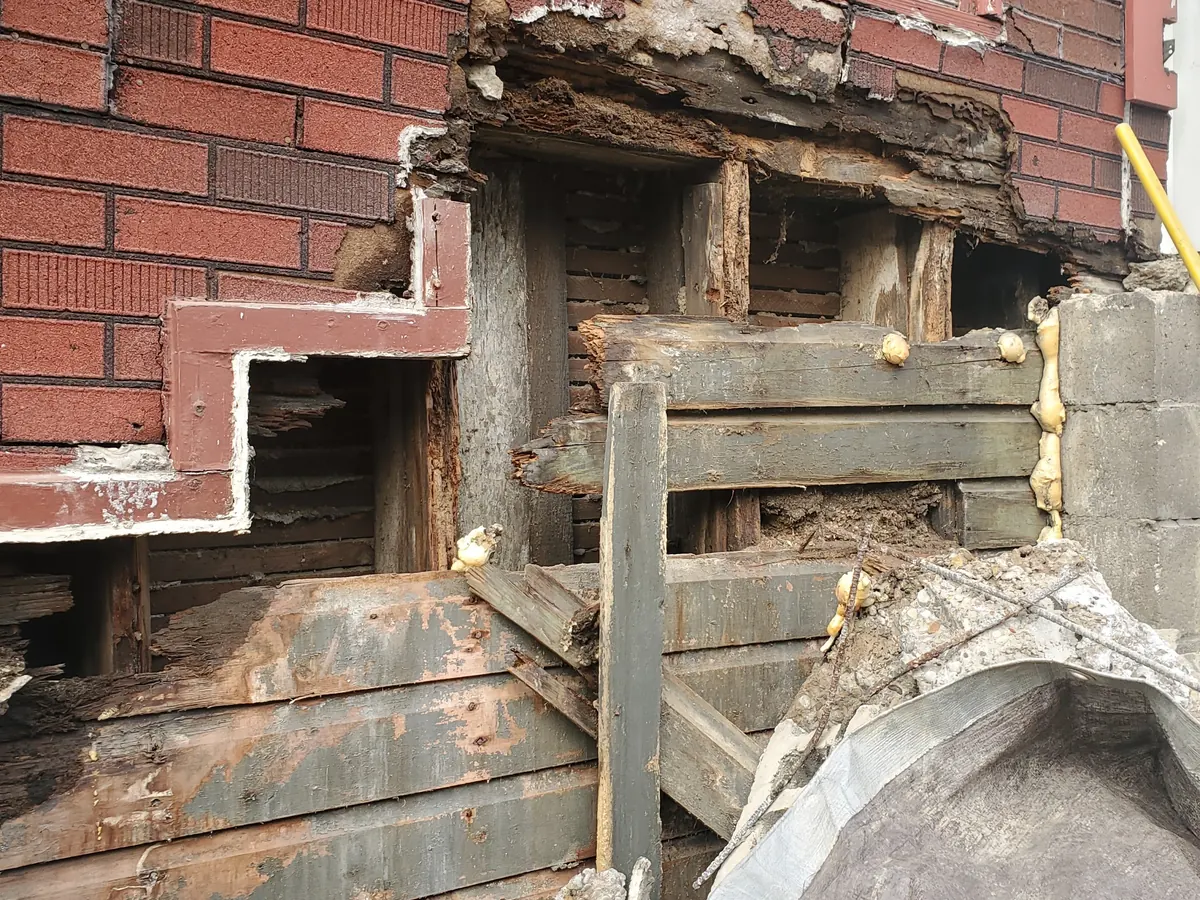 Base of a brick wall taken out at a doorway, exposing the rotted wood behind it