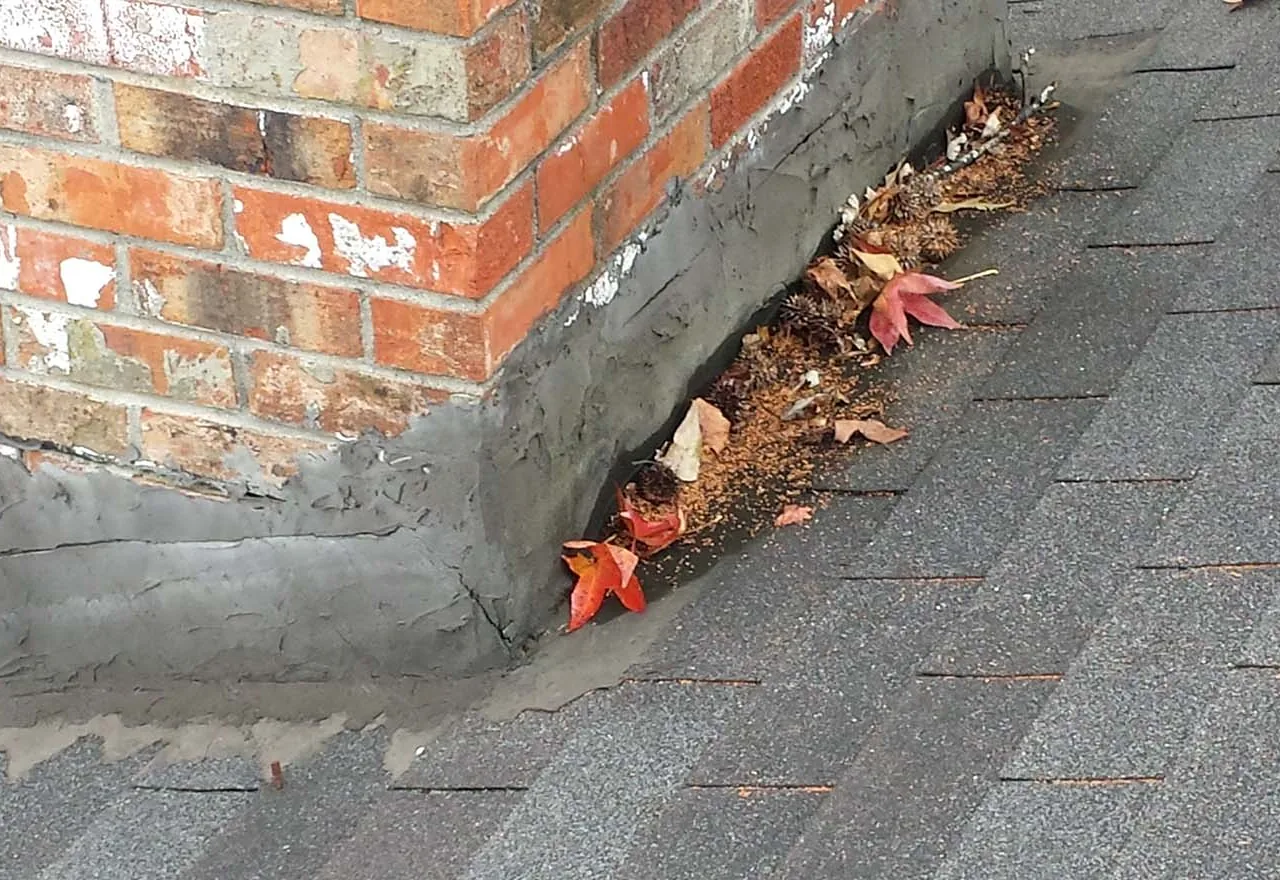 Fresh mortar crown worked in where a brick chimney meets the shingle roof