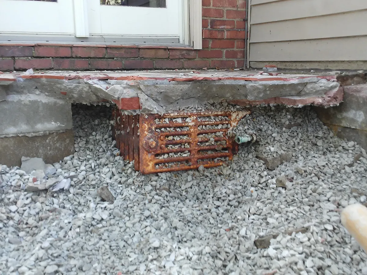 Old concrete slab broken out at a doorway threshold down to the stone below