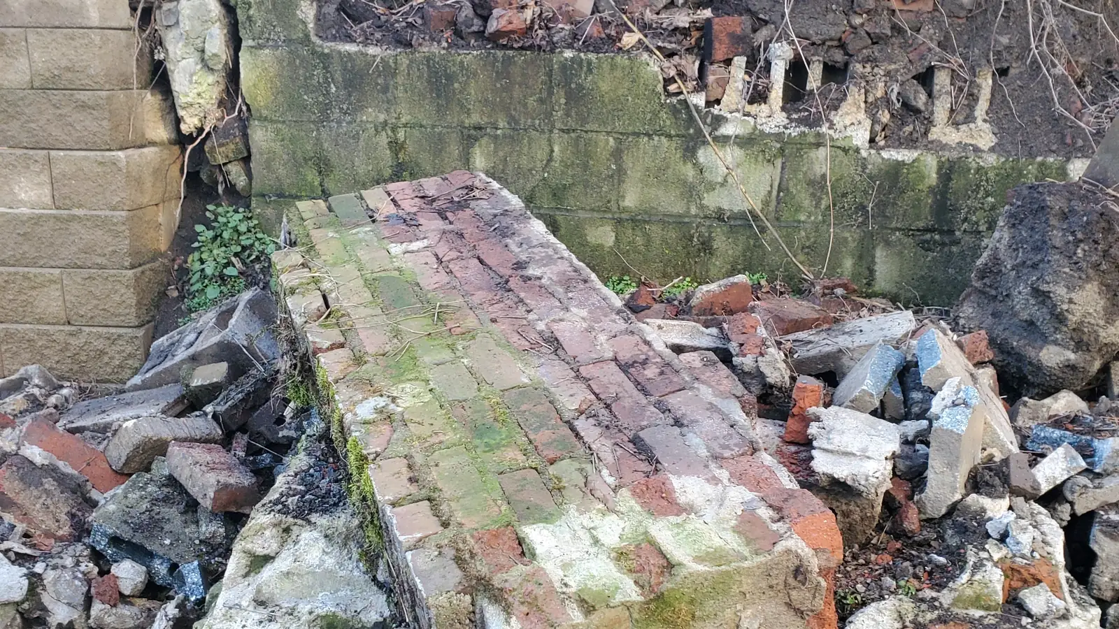 Failed brick retaining wall leaning out and breaking apart along its length