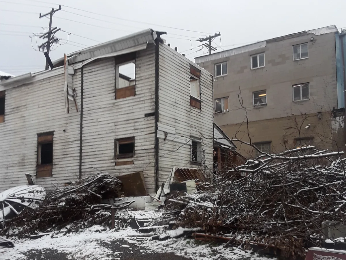 Frame house being torn down with the walls open and demolition debris stacked in the yard