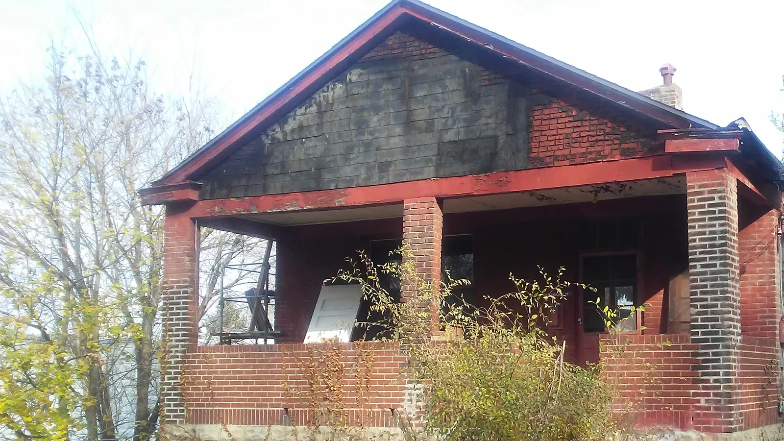 Vacant brick house with a covered porch standing ready for demolition in the Pittsburgh area