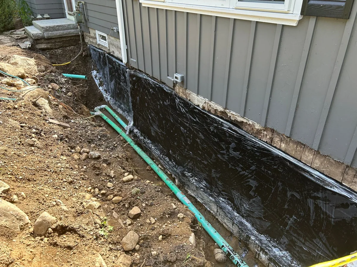 Excavated foundation wall coated with black waterproofing with the drain line laid alongside