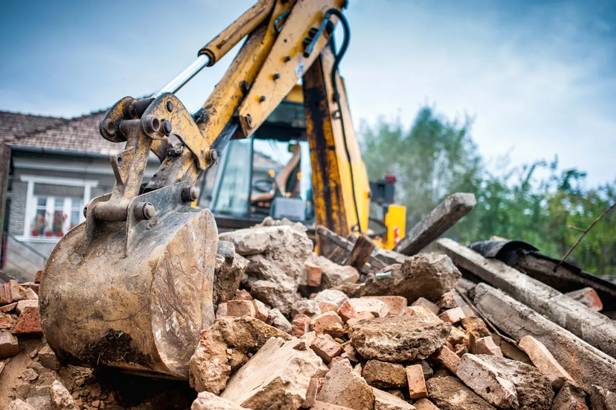 Excavator bucket resting on a pile of brick and concrete rubble from a demolished garage