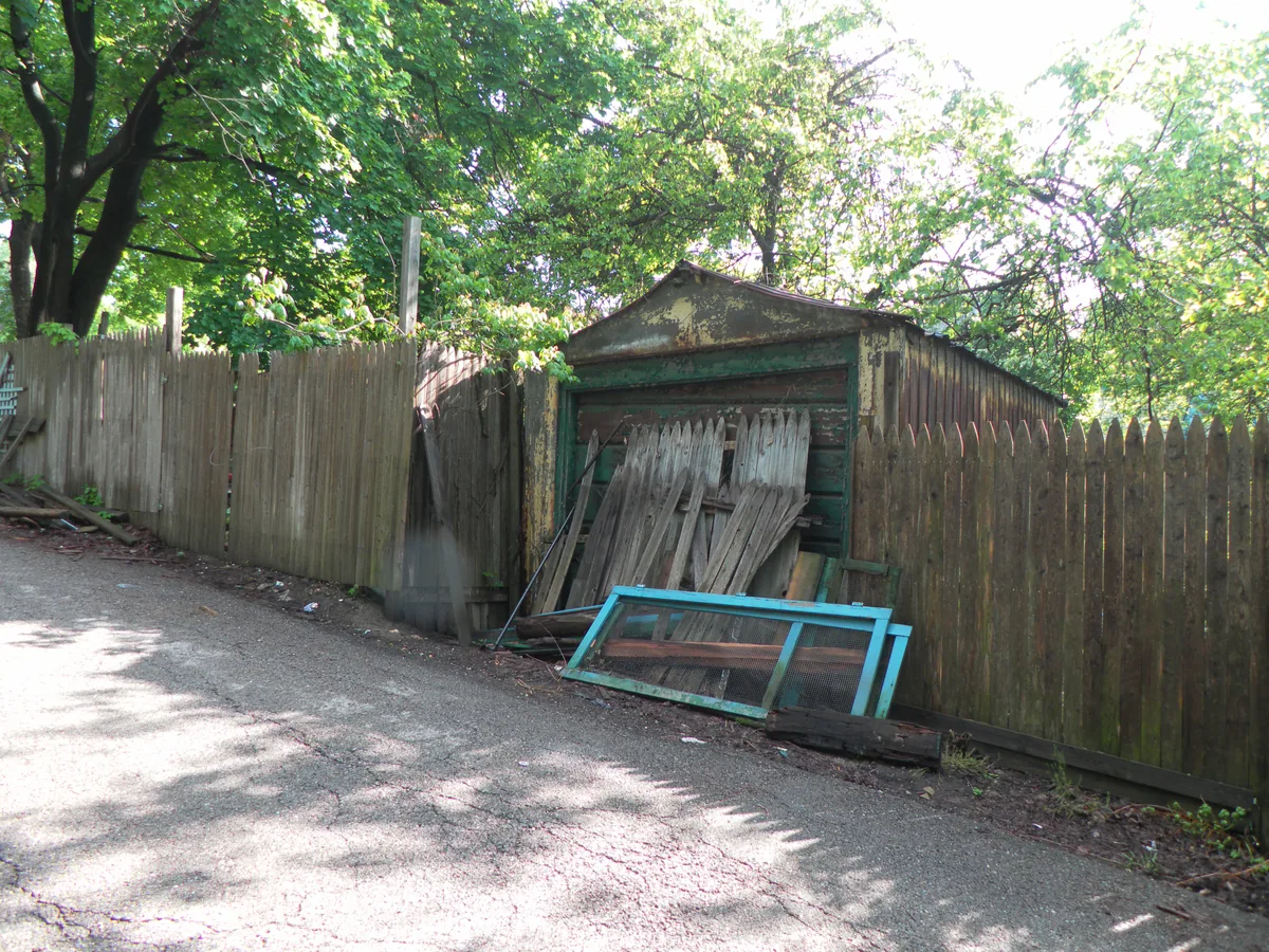 Leaning old frame garage behind a fence on a back alley