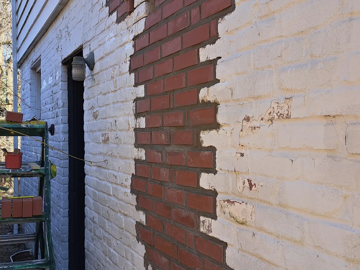 Section of a painted brick wall opened up and filled back in with new brick